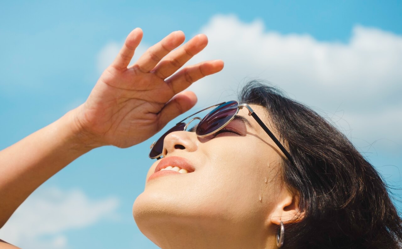 A woman shielding her face from the sun ray with sunglasses and her hand.