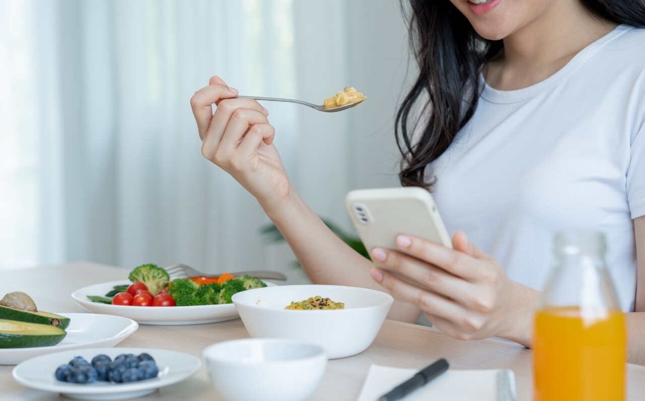 A woman eating while scrolling through her phone.
