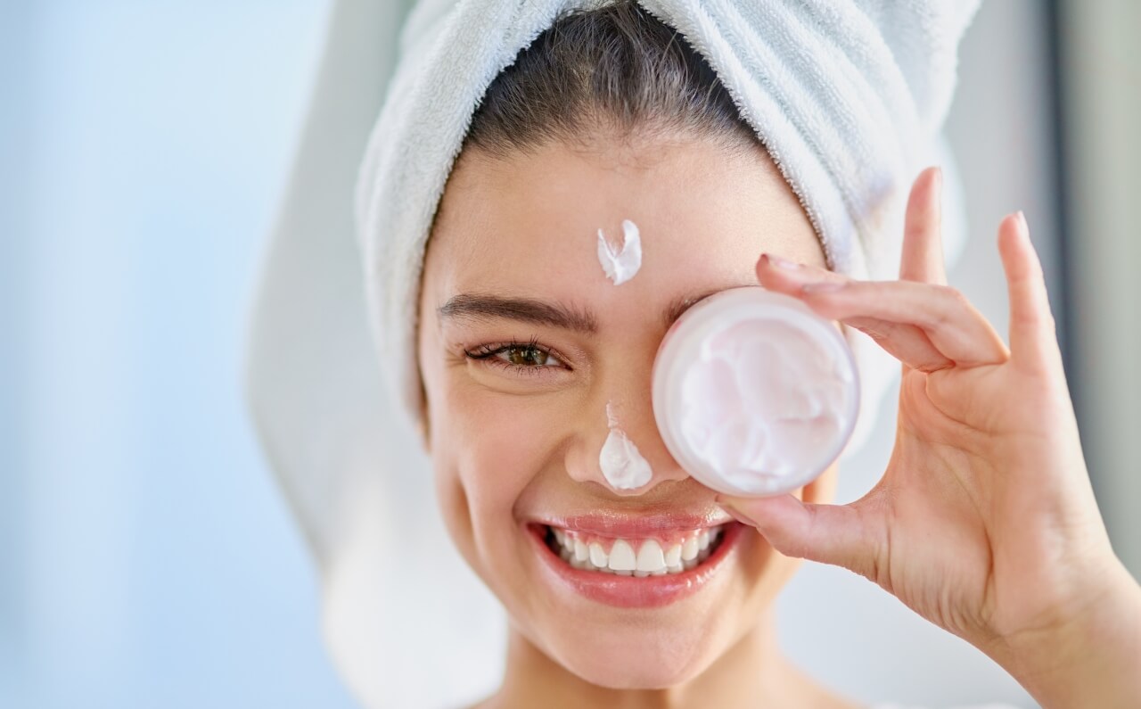 A woman with clear skin, smiling as she held a glass of facial cream.