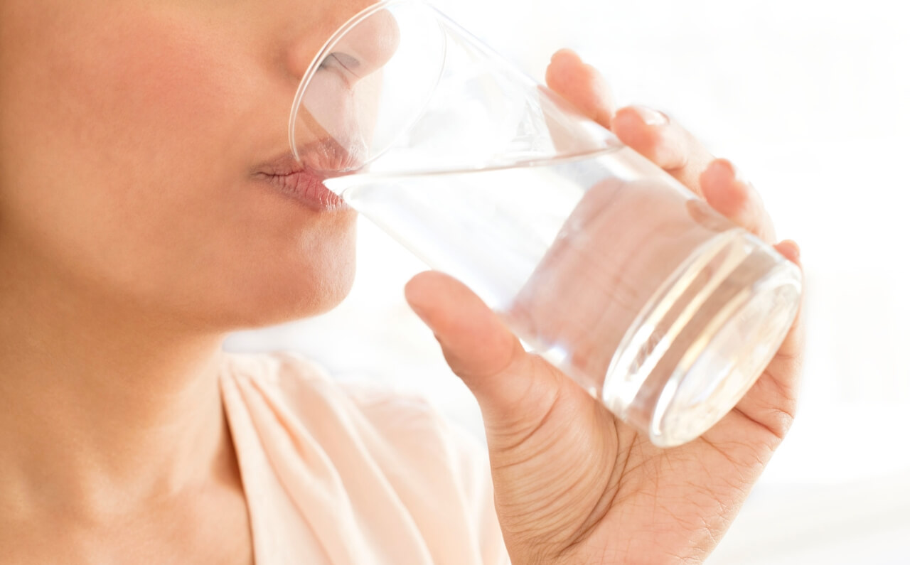 A woman sipping a glass of water, showing that practising healthy habits will lead to clear and acne-free complexion.