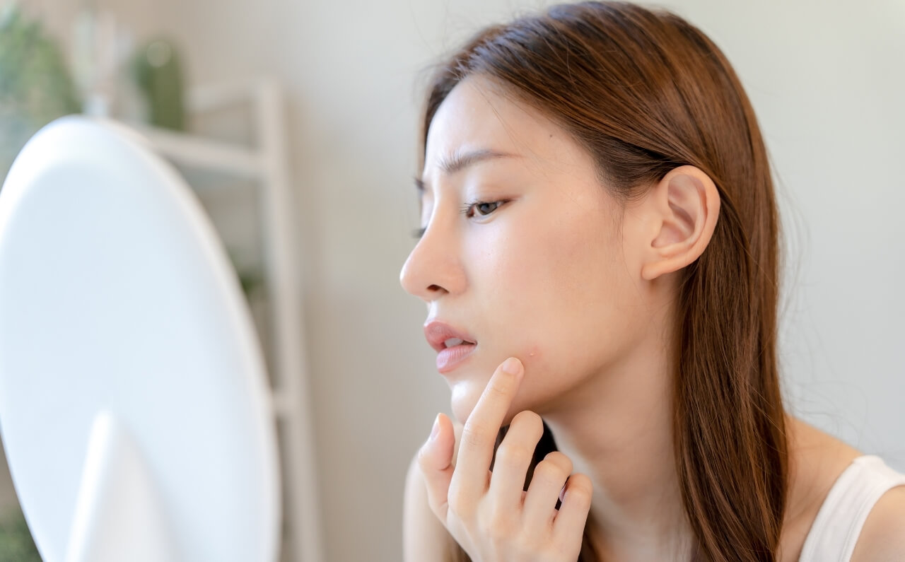 A woman touching her face. looking at her reflection in the mirror.