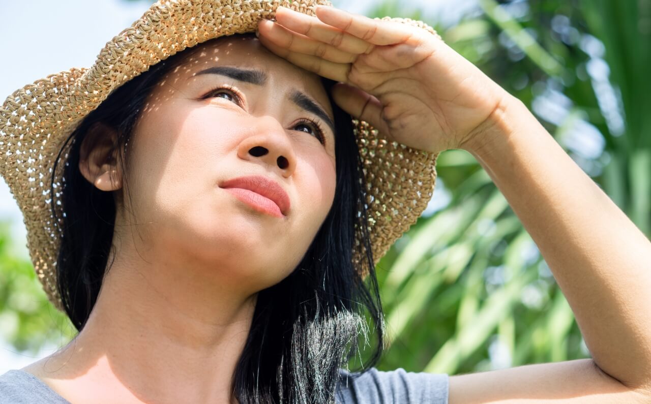 A woman wearing a hat, shielding her face with her hand to prevent exposure to the sun.