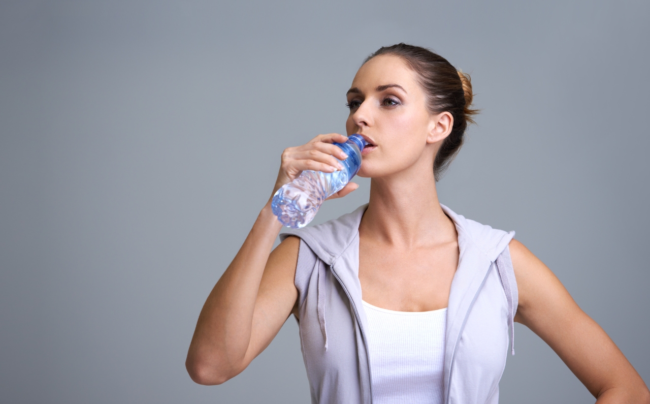 Woman in activewear drinking water to maintain skin hydration.