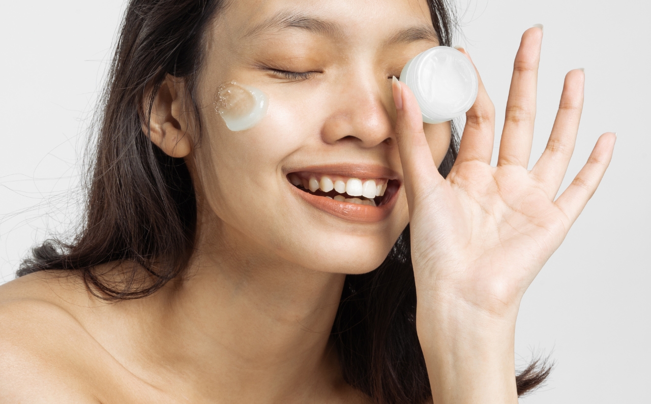 Woman smiling while holding a jar of facial cream, symbolising consistent skincare and HIFU-inspired natural V-shape face goals.