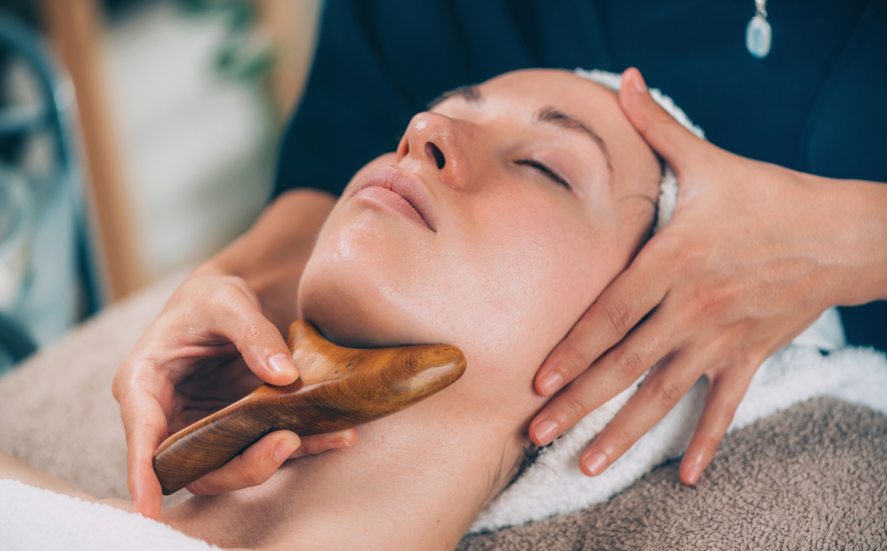 Aesthetician performing a facial massage with a tool on a relaxed woman to enhance natural V-shape face.