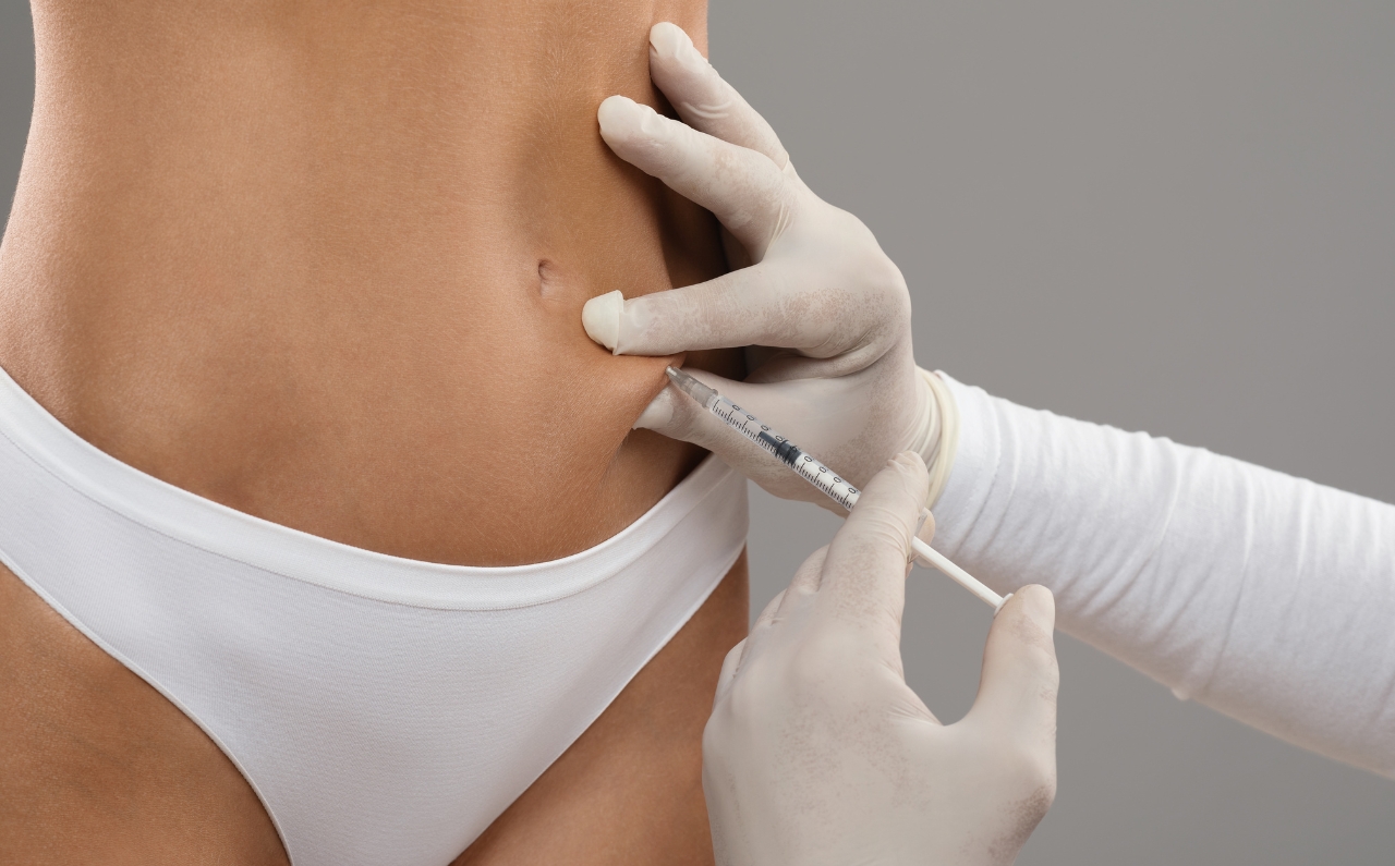 Aesthetician administering fat dissolving injection to a woman’s abdomen at an aesthetic clinic.
