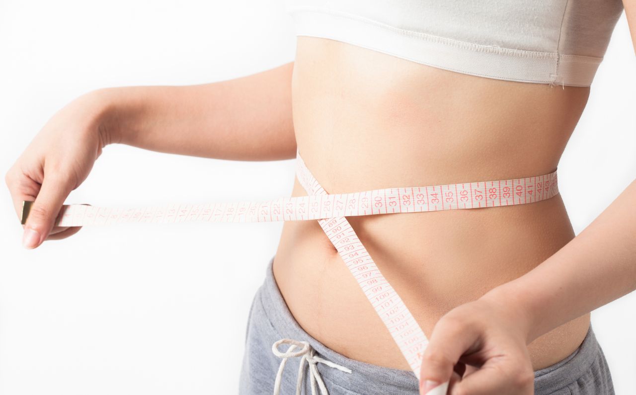 Woman measuring her waist with a tape measure, symbolising weight loss progress with Mounjaro® treatment at Millennium Clinic KL.