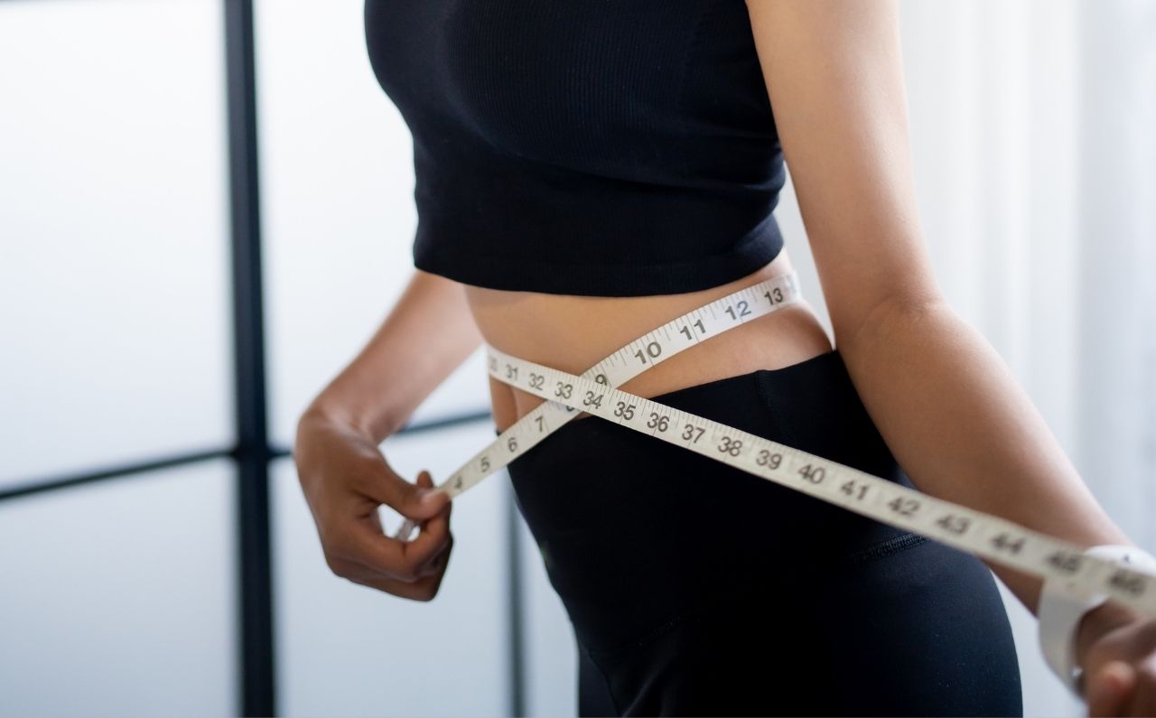 Woman measuring slim waist with tape measure, representing weight loss results with Wegovy® compared to traditional diet and exercise methods.