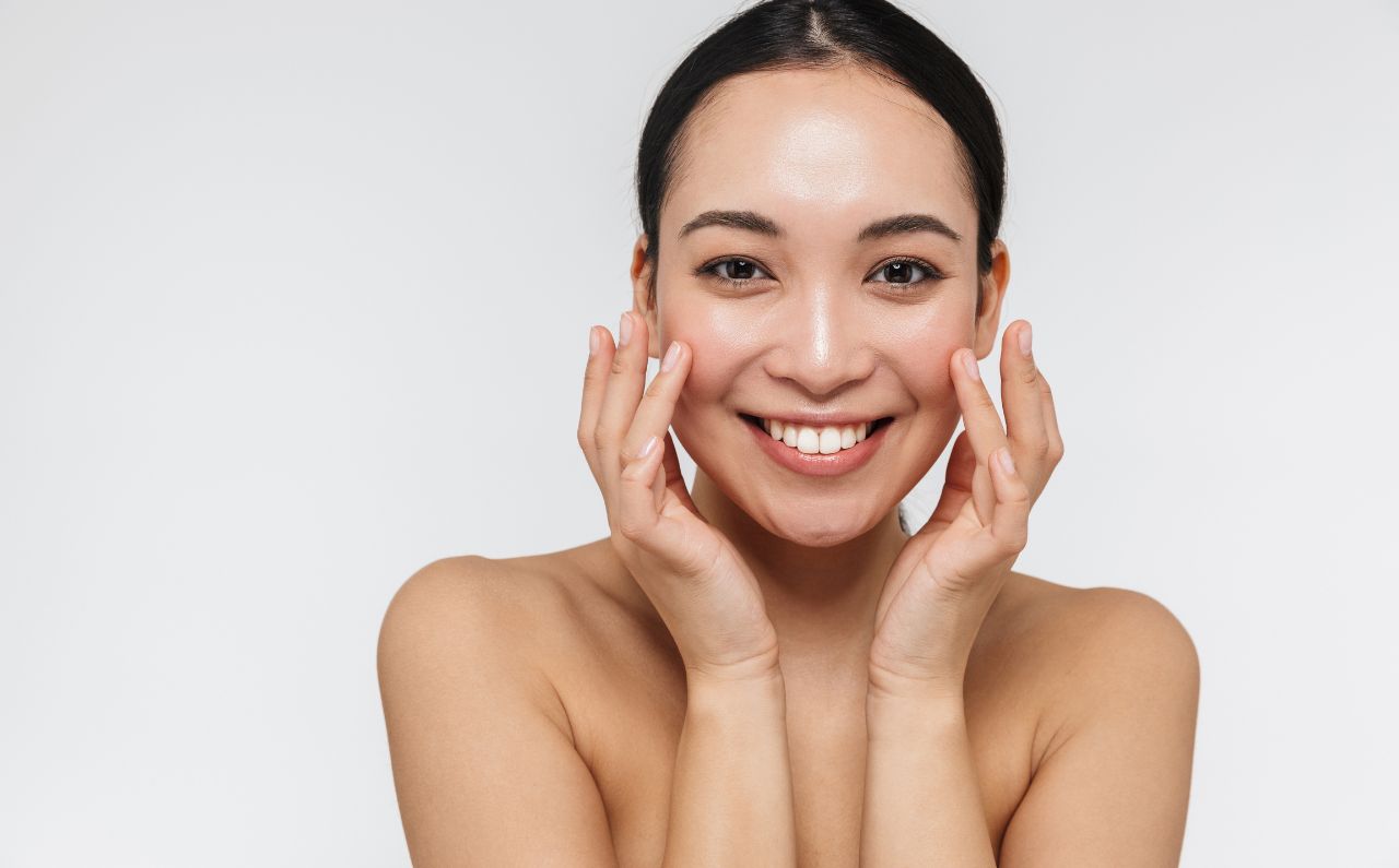 Woman smiling confidently while touching her smooth skin, representing the long-lasting, natural results of Radiesse treatment at Millennium Clinic KL.