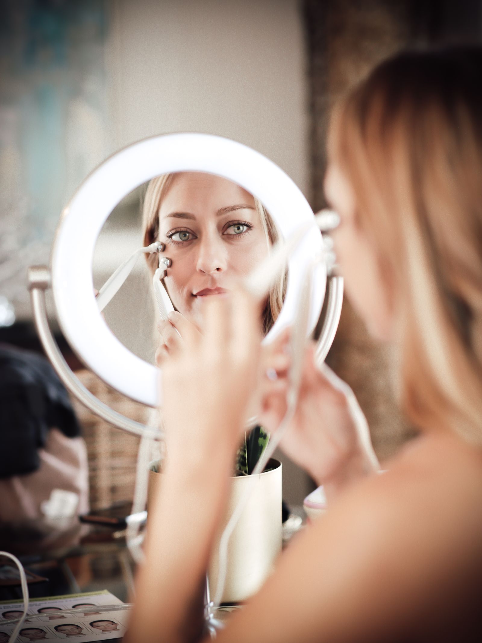 Woman reviewing her facial skin with a home beauty device in a mirror
